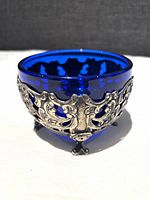 Close-up image of the deep blue glass bowl featuring the ornate silver stand with intricate decoration wrapped around it.