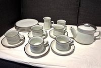 Photo showing entire tea set arranged including teapot, cups on saucers, side plates, creamer, and sugar bowl on white cloth background.