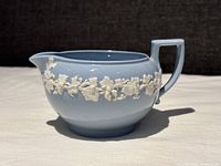 Side view of pale blue Wedgwood Queens Ware creamer showing white embossed grapevine detail and angular handle.