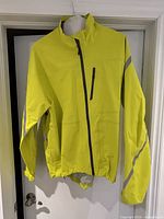 Front view of yellow cycling jacket showing full zipper, chest pocket, two side pockets, and reflective strip on right arm.