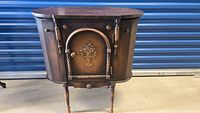 Full view of antique sewing cabinet showing curved top, carved floral design on front door, side doors, and slender legs.
