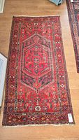 Full view of red Persian rug laid on wood floor