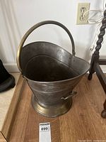 Angled side view of the brass ash bucket showing dented surface and arched handle.