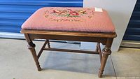 Full view of wooden bench with pink needlepoint seat showing floral embroidery and turned legs.