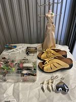 Photo showing beige ladies sandals, dress form jewelry stand dressed in beige satin, small shoe-shaped place card holders, and a plastic box with assorted jewelry items