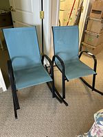 Front and angled view of two teal fabric outdoor rocking chairs with black metal frames inside a room, showing overall condition and design.