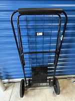 Front view of the folding metal shopping cart showing the grid frame and large rear wheels on a blue background.