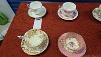 Four vintage teacups and saucers arranged on a red textured tablecloth showing floral and gold designs