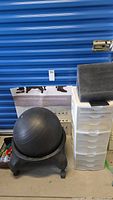 Photo showing exercise ball on wheeled stand next to white plastic utility drawer unit with multiple drawers.