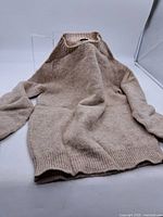 Full view of the beige wool sweater laid flat showing shape, sleeves, and ribbed neck, cuffs, and hem.