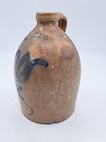 Full view of the antique crock jug showing its shape, handle, and front decoration.