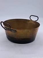 Full view of the antique copper pan showing round shape, iron handles, and patina on the copper surface.