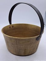 Front angle view showing round brass pot with iron handle upright.