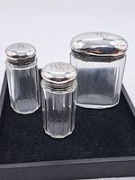 Overall view of three antique glass dresser bottles with silver lids showing monogram engraving.