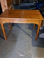Full view of rectangular wooden table with single drawer, showing the wood grain top and four straight legs.