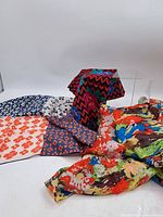 Image showing six assorted silk scarves with various floral and geometric patterns laid out and partly folded.