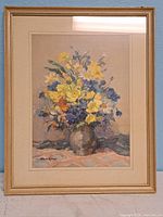 Framed print showing a bouquet of yellow, blue, orange, and white flowers in a vase with a light wood frame and cream mat.