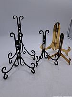 Photo showing all four frame/plate holders: two black metal stands with curled feet and two light wood stands with curved supports and hinged backs.
