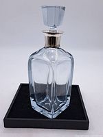 Front view of clear square glass decanter with faceted stopper on black platform
