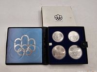 Opened case showing interior light blue satin, dark blue velour tray with four silver coins