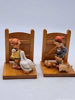 Front view of pair of Hummel bookends showing children figures and animals with wooden backings and bases.