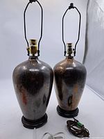 Pair of vintage lamps showing their overall shape, metallic bodies, harps, bulb sockets and round wooden bases with cords.