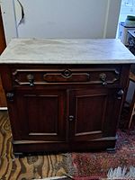 Front view of entire washstand showing marble top, wood base, drawer and cabinet doors.