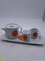 Full view of the complete tea set showing teapot, creamer, sugar bowl, and tray with retro orange circle decoration.