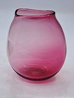 Full side view of the pink vintage art glass vase with curled rim and clear footed base.
