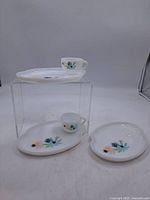 Overall view showing two cups and three plates/saucers, all decorated with floral patterns on white opaque glass.