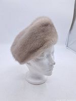 Side view of vintage fur hat on mannequin head showing rounded shape and dense light beige fur texture.