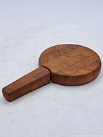 Round wooden cheese board with handle laying flat on white surface