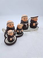 Group photo of all porcelain Hummel monk figurines with tray and spoon