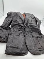 Full view of a black leather women's coat laid flat, showing the front with two flap pockets and chest pocket, button closure, and the coat's tailored styling.