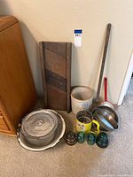 Various antique kitchen and household items including wooden washboard, UHL Pottery crock, baking pans, glass insulators, kraut cutter, and fireplace fork arranged on floor