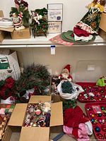 Photo showing wide array of Christmas items including wreaths, Santa dolls, boxes of glass ornaments, string lights, and angel tree topper on shelf.