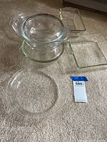 Photo showing all clear glass Pyrex bakeware items arranged on a carpeted floor: two round bowls with lids, one glass pie plate, and two rectangular baking dishes.