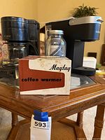 Mr. Coffee drip coffee maker and Maytag coffee warmer box on wooden table with glass top.