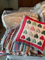 Comforters packed in plastic bags, decorative heart patchwork pillow, and colorful woven throw rugs stacked.