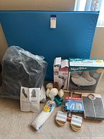 Photo showing large blue foldable yoga mat, various boxed and loose fitness and massage related items including dumbbells, hand weights, jump rope, and scale.