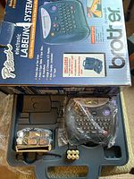 Brother P-Touch electronic labeling system in carrying case with accessories including batteries and tape cassettes, appearing new in packaging and plastic wrapping.