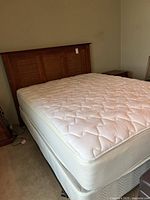 Photo of queen Simmons mattress on box spring with wooden paneled headboard.