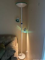 Full view of the 6-foot tall white halogen floor lamp placed beside a couch, showing the main lamp shade on top and a smaller adjustable spotlight arm in the middle.