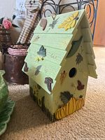 Photo of a pastel green wooden decorative birdhouse painted with fall leaves and pumpkins.