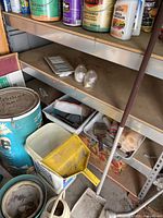 Photo of metal shelving with paint cans, paint brushes, a yellow scoop, and other small items