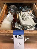 Top view of an open wooden drawer filled with various kitchen tools including a handheld electric mixer and wooden handled utensils.