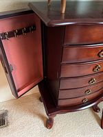 Close-up of the jewelry chest side door open showing hooks for hanging necklaces and shelves inside.