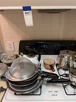 Cookware items on stove including pots, pans, teapot, egg poachers, and lids