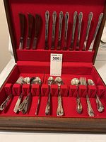 Photo of silverware set inside wooden box with red lining showing knives, forks and spoons arranged in compartments