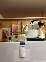Vintage Sunbeam Mixmaster stand mixer on top of white refrigerator, alongside a box and other kitchen items